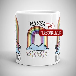 May include: White ceramic mug featuring a colorful rainbow design with the name "ALYSSA" above it. The word "PERSONALIZED" is in a red rectangle. The mug also has a unicorn and the words "LET IT GO".