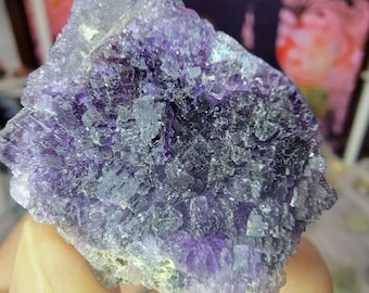 May include: A large, purple fluorite crystal with a cluster of smaller crystals. The crystal has a sparkly, iridescent surface.