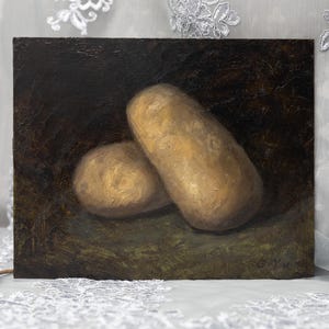 Puede incluir: Pintura al óleo de dos patatas, una alargada y otra redonda, sobre un fondo oscuro y texturizado. Las patatas están pintadas en tonos marrones y beige, con reflejos de luz. La obra evoca un tema de bodegón.
