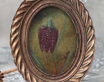 May include: Oval framed painting of a purple flower with green stems against a gold background. The frame is a detailed, ornate bronze color. The artwork is a botanical theme.