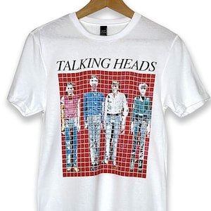May include: White t-shirt with a graphic print of the band Talking Heads. The band members are standing in a grid pattern against a red background. The band's name is printed in black above the image.