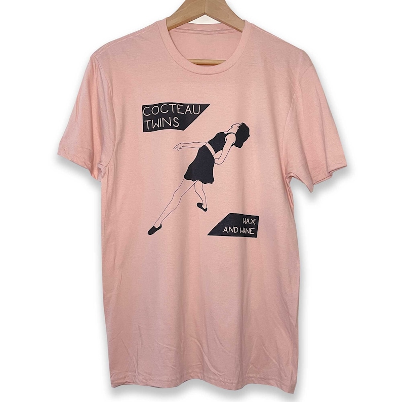 May include: A pink t-shirt with a black and white graphic print of a woman in a dress. The graphic includes the text "Cocteau Twins" and "Wax and Wane".
