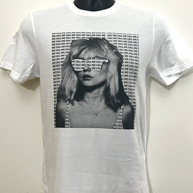 May include: White t-shirt with a black and white image of a woman wearing sunglasses with the text "Call Me Call Me Call Me Call Me" repeated across the sunglasses.