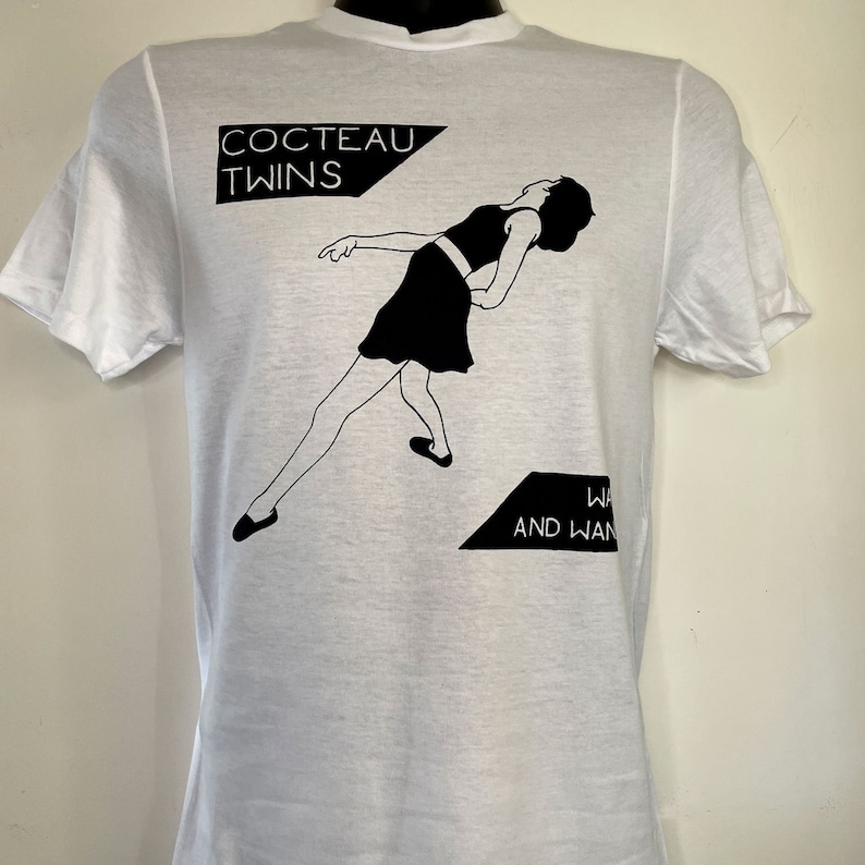 May include: White t-shirt with a black and white graphic print of a woman in a skirt and the text "Cocteau Twins" and "Wilderness and Wanderlust".