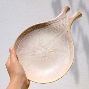 hand holding ceramic beige plate with geometric pattern and two handles