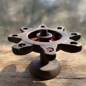 May include: A black ceramic candle holder with eight candle slots and a central, raised, circular platform. The candle holder has a starburst design and a red glaze on the inner rim of the candle slots.