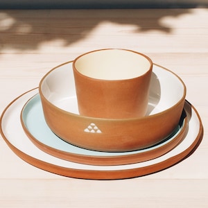 Natural red clay round plates with white, turquoise and yellow glazes inside on a light wood table.