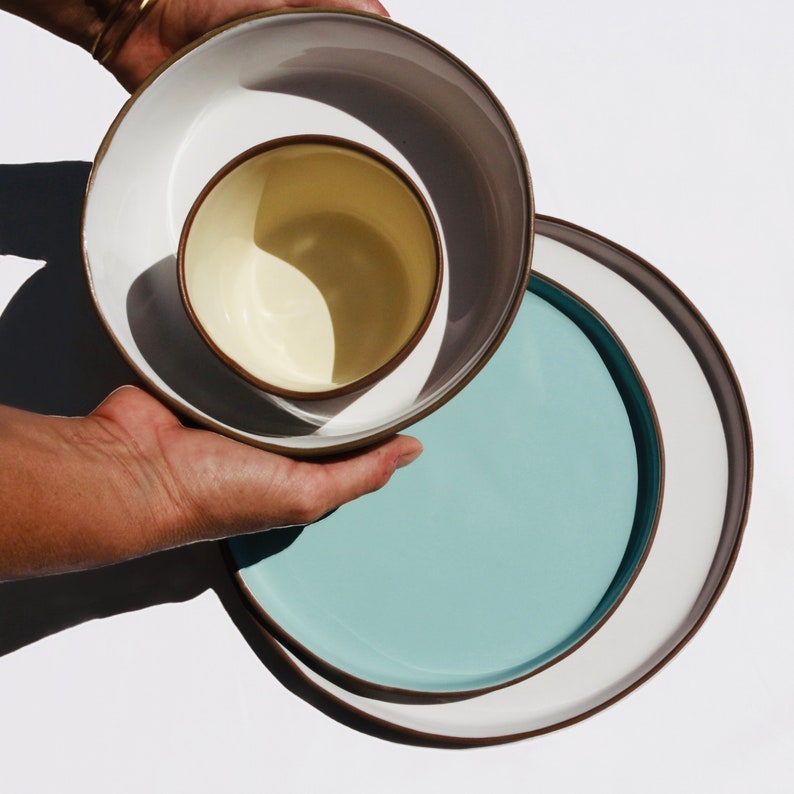 Hand holding medium bowl and plate on a white background.