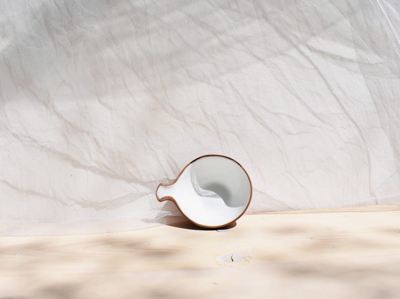May include: A white ceramic pitcher with a brown rim, resting on a light wood surface. The pitcher is tilted slightly, revealing the inside.