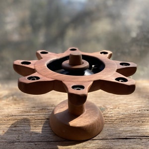 May include: A wooden candle holder with a starburst design and a black center. The holder has eight candle slots and a round base.