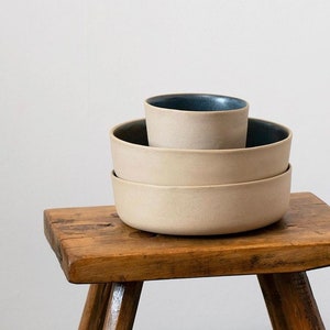 Two bowls and a cup in sand clay with dark blue glazed on a dark wood stool