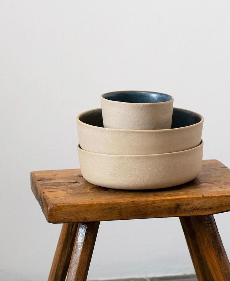Two bowls and a cup in sand clay with dark blue glazed on a dark wood stool