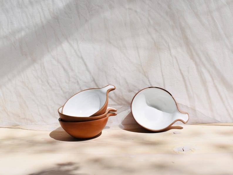 May include: Four white ceramic bowls with brown rims and handles. The bowls are stacked in a pile of two, with one bowl on its side.