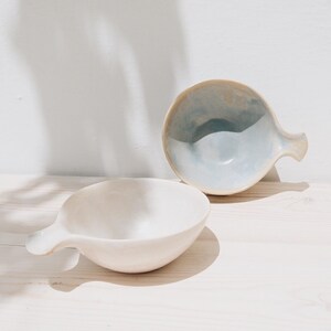 May include: Two ceramic bowls with handles. One bowl is white and the other is light blue with a white interior.