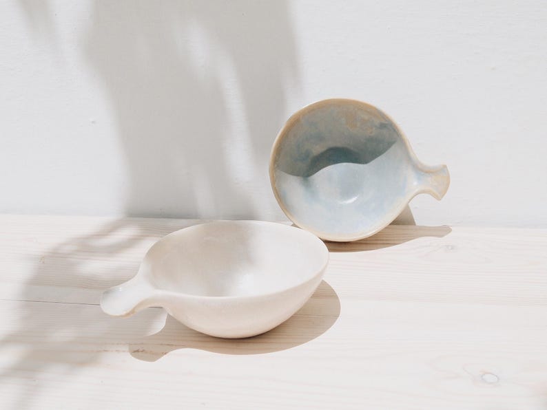May include: Two ceramic bowls with handles. One bowl is white and the other is light blue with a white interior.