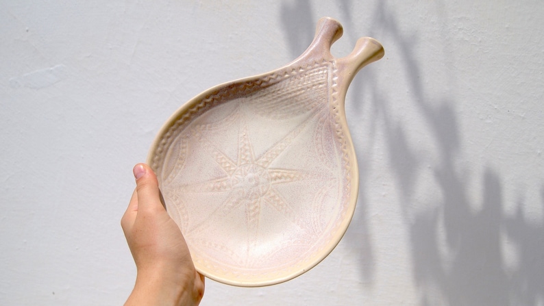 hand holding ceramic beige plate with geometric pattern and two handles