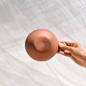 May include: A terracotta bowl with a circular design on the bottom. The bowl is being held by a hand.
