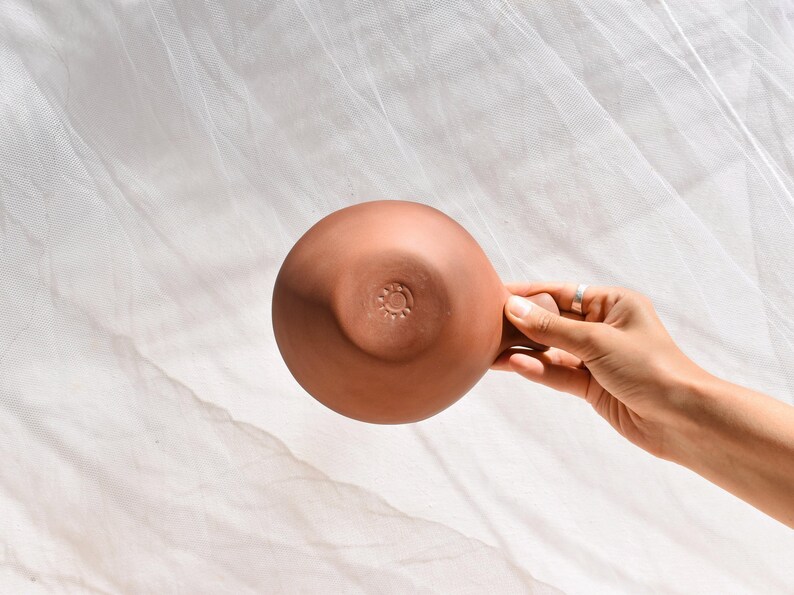 May include: A terracotta bowl with a circular design on the bottom. The bowl is being held by a hand.