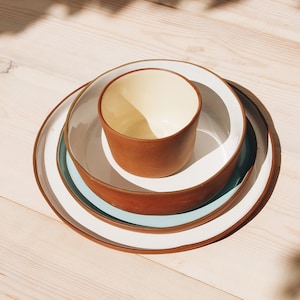 Natural red clay round plates with white, turquoise and yellow glazes inside on a light wood table.