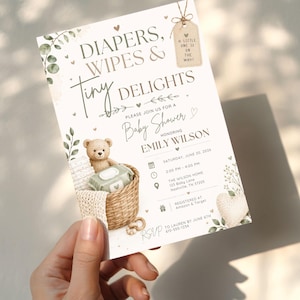 May include: A rectangular baby shower invitation card featuring the text Diapers, Wipes & Tiny Delights, a brown teddy bear in a woven basket, green leaves, and a small tag reading A Little One Is On The Way, with event details for Emily Wilson.