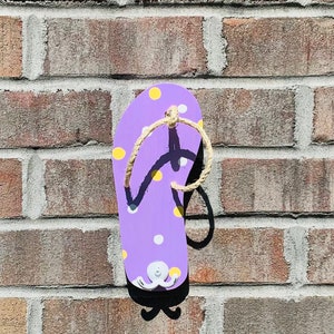 May include: Purple flip flop with yellow and white polka dots, a white octopus, and a rope handle. The flip flop is mounted on a brick wall.