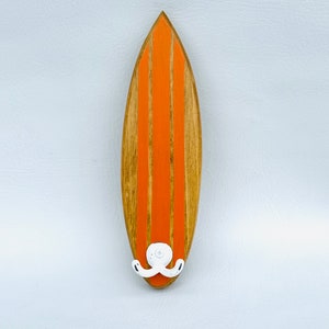 May include: Orange and brown wooden surfboard wall hook with a white octopus design.