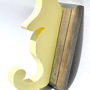May include: A yellow wooden seahorse wall hook with a brown wooden base. The hook is shaped like a seahorse with a curled tail.