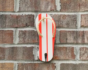 Puede incluir: Un gancho de pared con forma de chancla de rayas rojas y blancas con un detalle de cuerda.