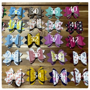 May include: A collection of 44 handmade hair bows in various colors and patterns, including floral, polka dot, and geometric designs. Each bow is numbered from 25 to 44.