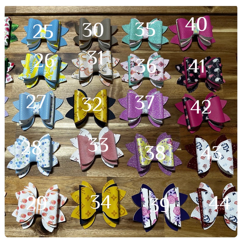 May include: A collection of 44 handmade hair bows in various colors and patterns, including floral, polka dot, and geometric designs. Each bow is numbered from 25 to 44.