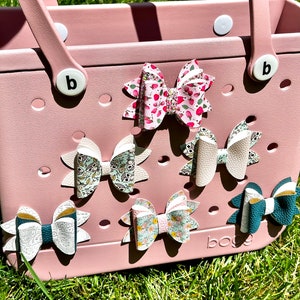 May include: A pink tote bag with a white handle and a white letter "b" on the side. The bag has a grid of holes and is decorated with six colorful fabric bows.