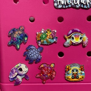 May include: A pink plastic tote bag with a variety of colorful turtle stickers. The stickers feature different designs, including a turtle with a flower crown, a turtle with a seashell, and a turtle with a beach scene.