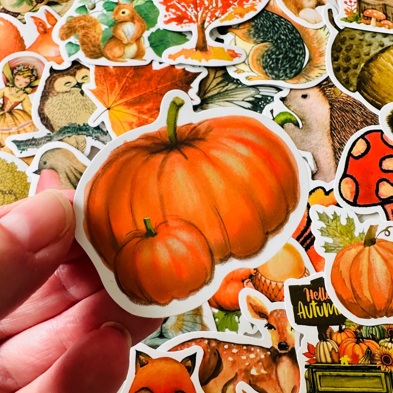 Op de afbeelding: Een set herfst-stickers met pompoenen, eekhoorns, bladeren en een hert. De stickers zijn gedrukt op wit papier met een glanzende afwerking.