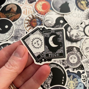 May include: Two black and white tarot cards with illustrations of the sun and moon. The sun card has the Roman numeral XIX and the text "Sun" at the bottom. The moon card has the Roman numeral XVIII and the text "Moon" at the bottom.