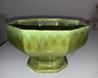 May include: A green ceramic planter with a hexagonal shape and a scalloped rim. The planter has a base with a hexagonal shape.