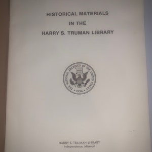 May include: A black and white image of a book cover with the title "Historical Materials in the Harry S. Truman Library". The cover also includes the National Archives seal and the text "Harry S. Truman Library, Independence, Missouri, November 1984."
