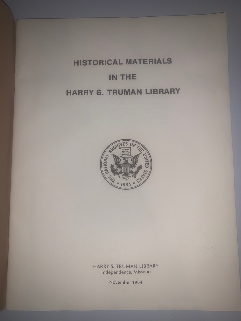 May include: A black and white image of a book cover with the title "Historical Materials in the Harry S. Truman Library". The cover also includes the National Archives seal and the text "Harry S. Truman Library, Independence, Missouri, November 1984."