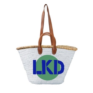 Könnte beinhalten: Weiße geflochtene Tragetasche mit braunen Ledergriffen und einem grünen Kreis mit den Buchstaben "LKD" in Blau.