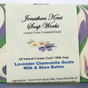 May include: A bar of lavender chamomile goat's milk soap with shea butter. The soap is white with green and purple swirls. The label reads "Jonathan Kent Soap Works, Luxury From Contented Goats, All Natural Creamy Goat's Milk Soap, Lavender Chamomile Goats Milk & Shea Butter, Ingredients: Farm Fresh Goats Milk, Saponified Oils of", and lists the ingredients.