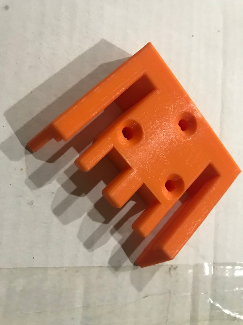 May include: Orange plastic 3D printed part with four holes and a series of slots. The part is designed to be attached to another object.