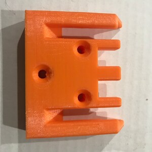 May include: Orange plastic 3D printed part with three slots and three holes.