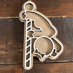 May include: A wooden cutout ornament of a gingerbread person hanging from a candy cane. The gingerbread person is upside down with a bow tie and a smiling face.
