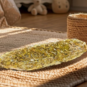Peut inclure: Un plateau en verre de forme oblongue avec un motif de feuilles d'or. Le plateau est rempli d'un matériau doré texturé et repose sur un tapis tissé. Un panier tressé est en arrière-plan.