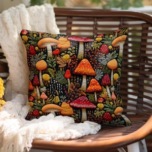 Faux embroidered mushroom pillow covers. Mushrooms are red, orange, and yellow on a black background. They are surrounded by ferns and berries.