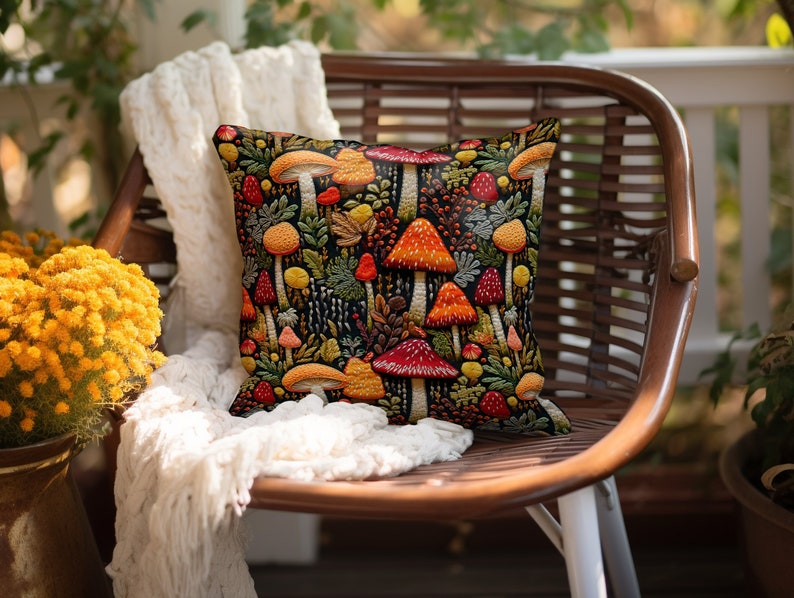 Faux embroidered mushroom pillow covers. Mushrooms are red, orange, and yellow on a black background. They are surrounded by ferns and berries.