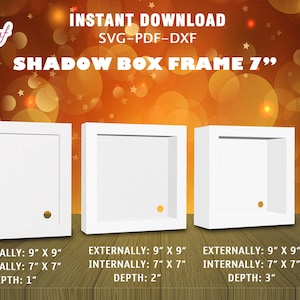 Puede incluir: Tres marcos de caja de sombra blancos, cada uno con una profundidad diferente: 2,5 cm, 5 cm y 7,5 cm. Los marcos miden 23 cm por 23 cm externamente y 18 cm por 18 cm internamente. Los marcos están sobre una superficie de madera.