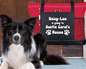 May include: A black and white border collie dog sits in front of a red and black tote bag. The bag has the text "Daisy-Loo is going to Auntie Carol's House" with paw prints on either side.