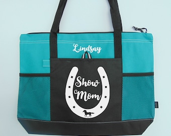 May include: Teal and black tote bag with a horseshoe and the words "Show Mom" in white. The bag has a zippered top and a mesh pocket on the side. The name "Lindsay" is embroidered on the front of the bag.