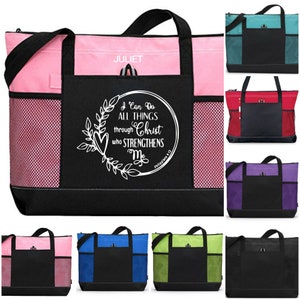 May include: A black and white tote bag with a zipper closure and a mesh pocket. The bag has a white design that says "I can do all things through Christ who strengthens me" with a heart and leaves. The bag is available in pink, red, teal, purple, blue, green, and black.