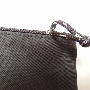 Peut inclure: Gros plan d'un sac &agrave; cordon noir avec une fermeture &eacute;clair et un cordon blanc et noir. Le sac est fait d'un tissu r&eacute;sistant.